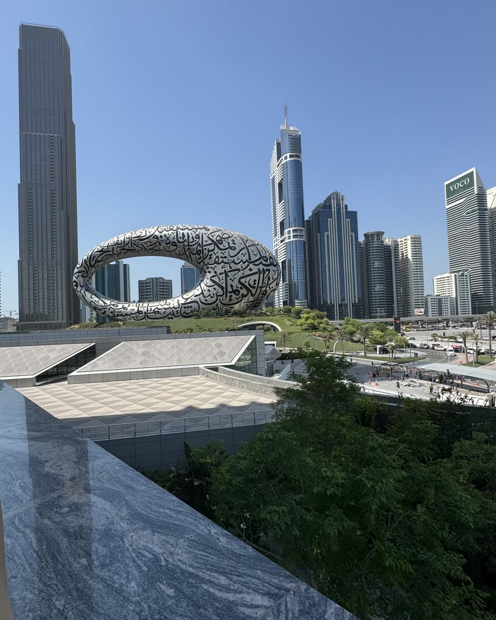 The Museum of the Future in Dubai by day, with trees and a marble ledge in the foreground